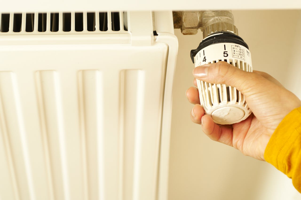 about-01 Close-up of hand adjusting radiator thermostat to control home heating temperature.