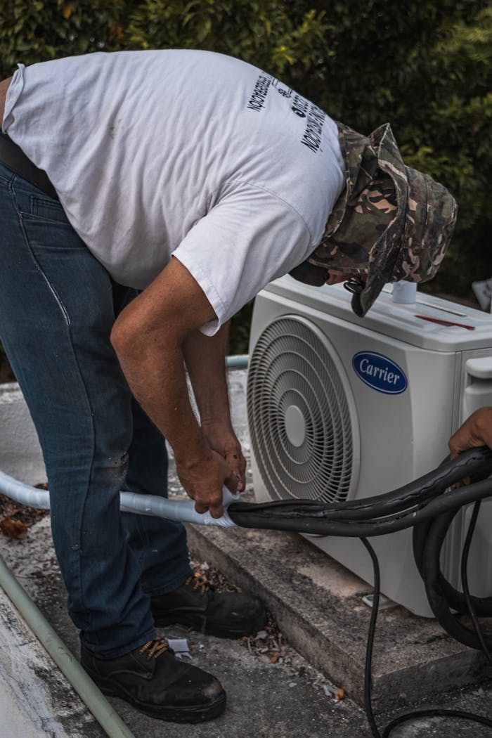 gallery-3 A technician performs maintenance on an outdoor air conditioning unit, focusing on hose connections.